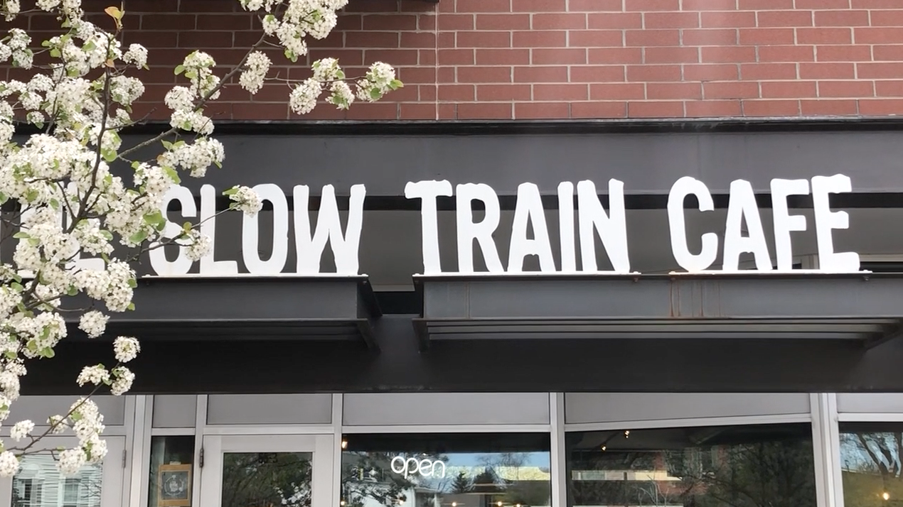 Store sign reading "Slow Train Cafe" on red brick building.