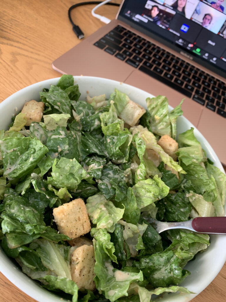 This is an image of a caesar salad, sans chicken, on a table next to a computer.