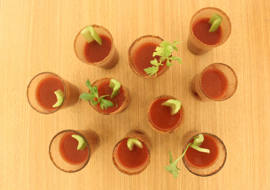 Ten homemade bloody marys on a dining room table, garnished with celery.