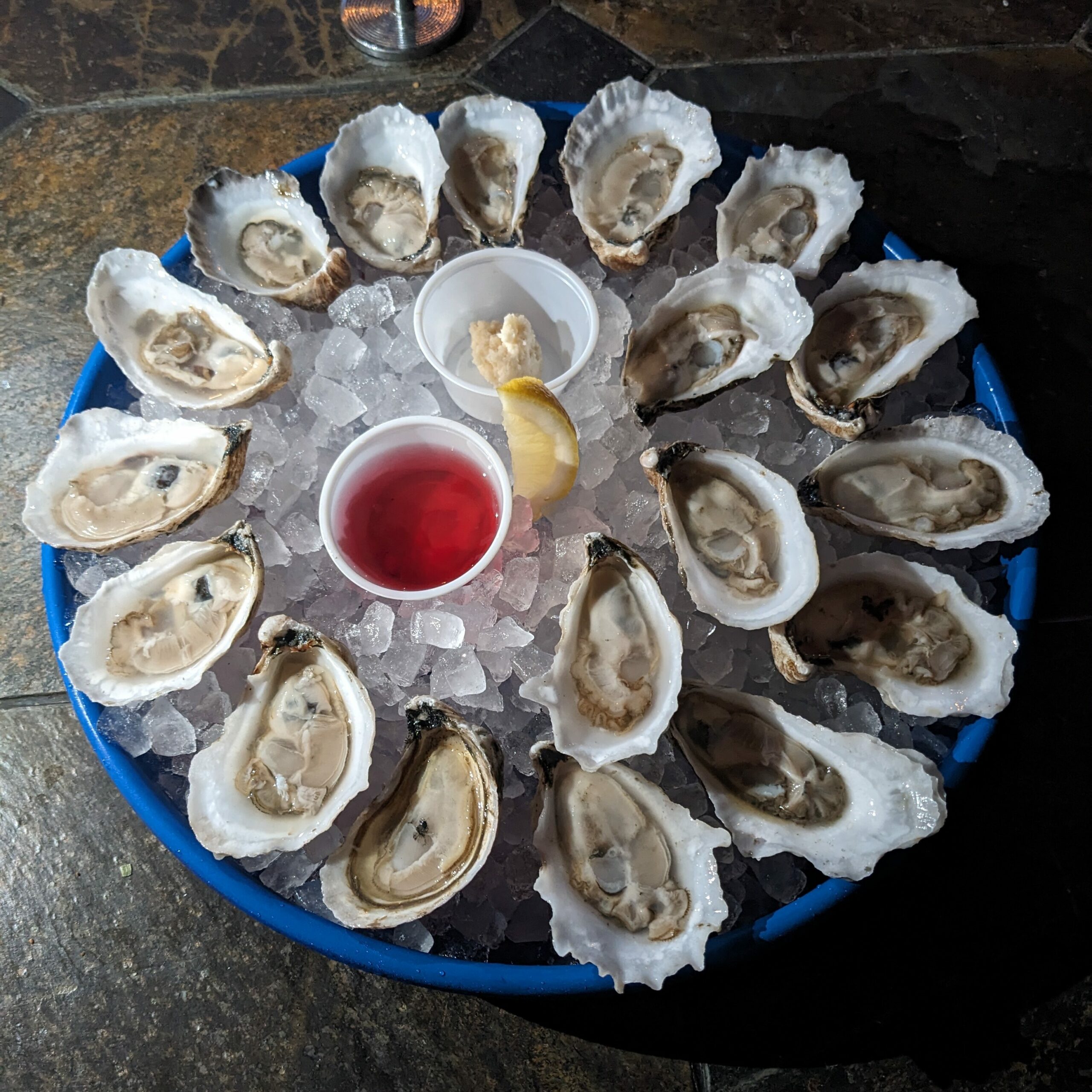 a photo of a dozen and a half oysters on the half shell, served on ice with lemon, horseradish, and red wine vinegar.