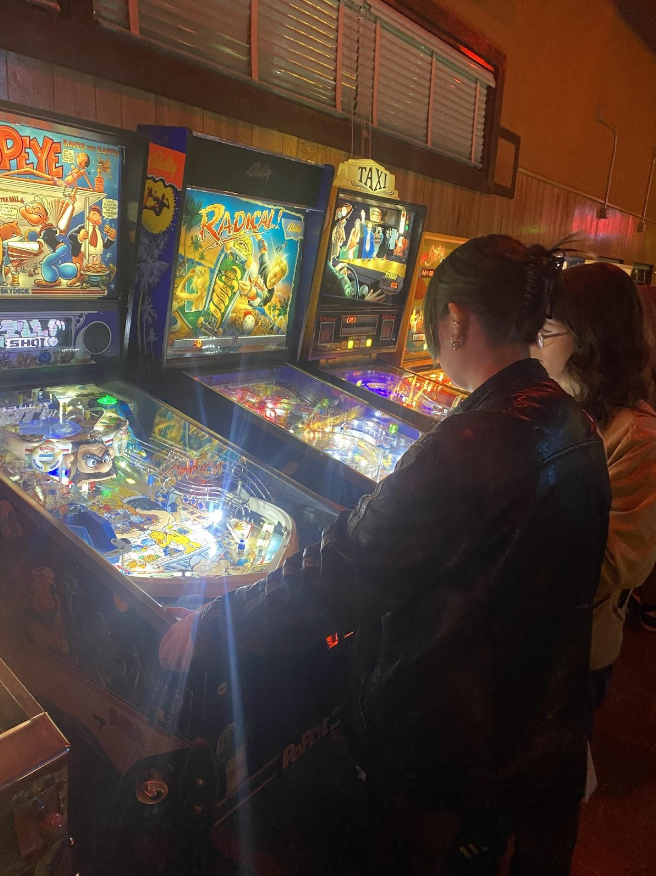Two people standing next to each other playing pinball