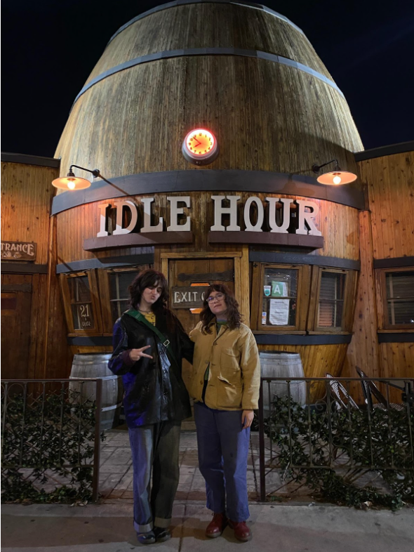 two people in front of a barrel-shaped building with a sign reading “Idle Hour”