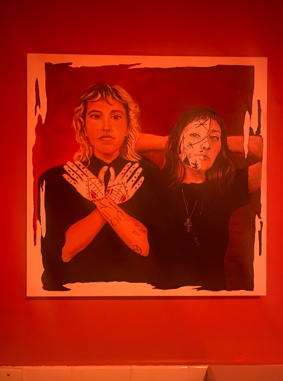Paining of a blond woman with hands crossed making an “x” next to brunette woman with hands on her head, both wearing black