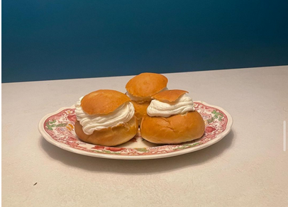  This image is of three semlor made by the author on a ceramic plate, they are not symmetrical and have different cream to pastry ratios. A portion of the top of the sweet bun has been cut off and put on top of the cream as a sort of hat<br>