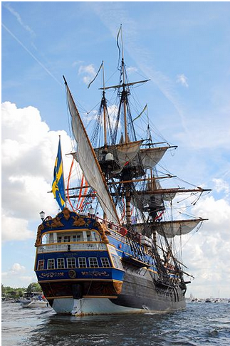 This image is of a recreated Swedish East India trading vessel, it is a large boat with three main sails. It has multiple windows and cannon holes with no cannons in them. <br>