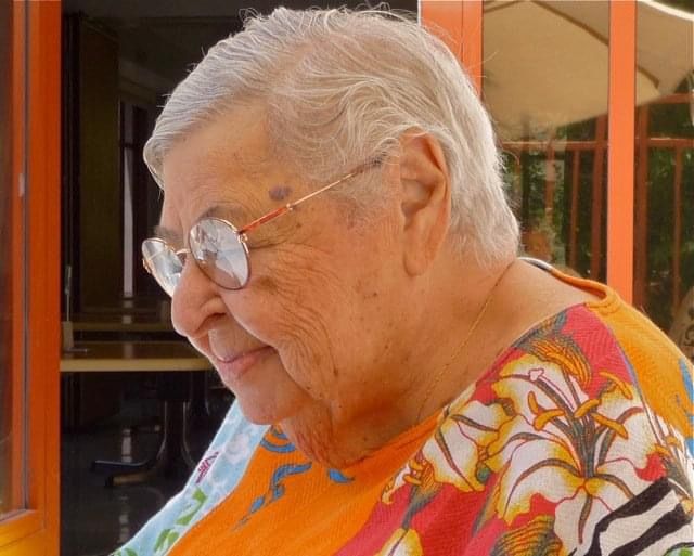 Side profile of an elderly woman with short hair, glasses, and a floral shity