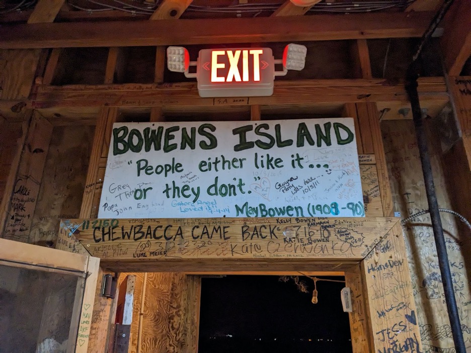 The particleboard sign above a door at Bowens Island painted with the text “Bowens Island: “people either like it…or they don’t,” May Bowen (1909-90)”. The sign and walls around it are signed in sharpie with names of visitors and the dates they dined at the restaurant.