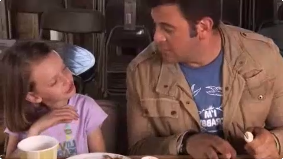 The author, left, with a lavender shirt and side parted shoulder-length hair, speaks to Adam Richman, who is listening and holding a shucking knife.